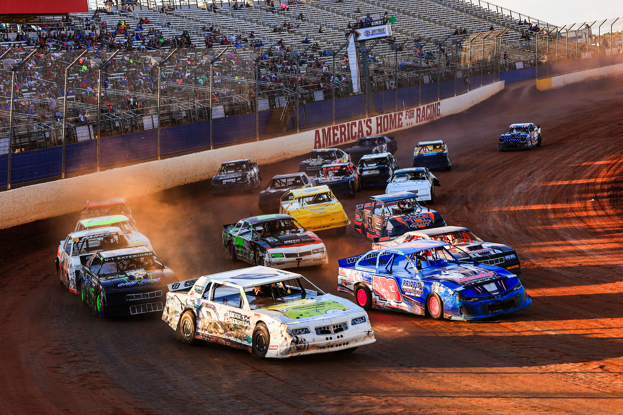 A pack of Street Stock drivers racing their cars around The Dirt Track at Charlotte during the World Short Track Championship